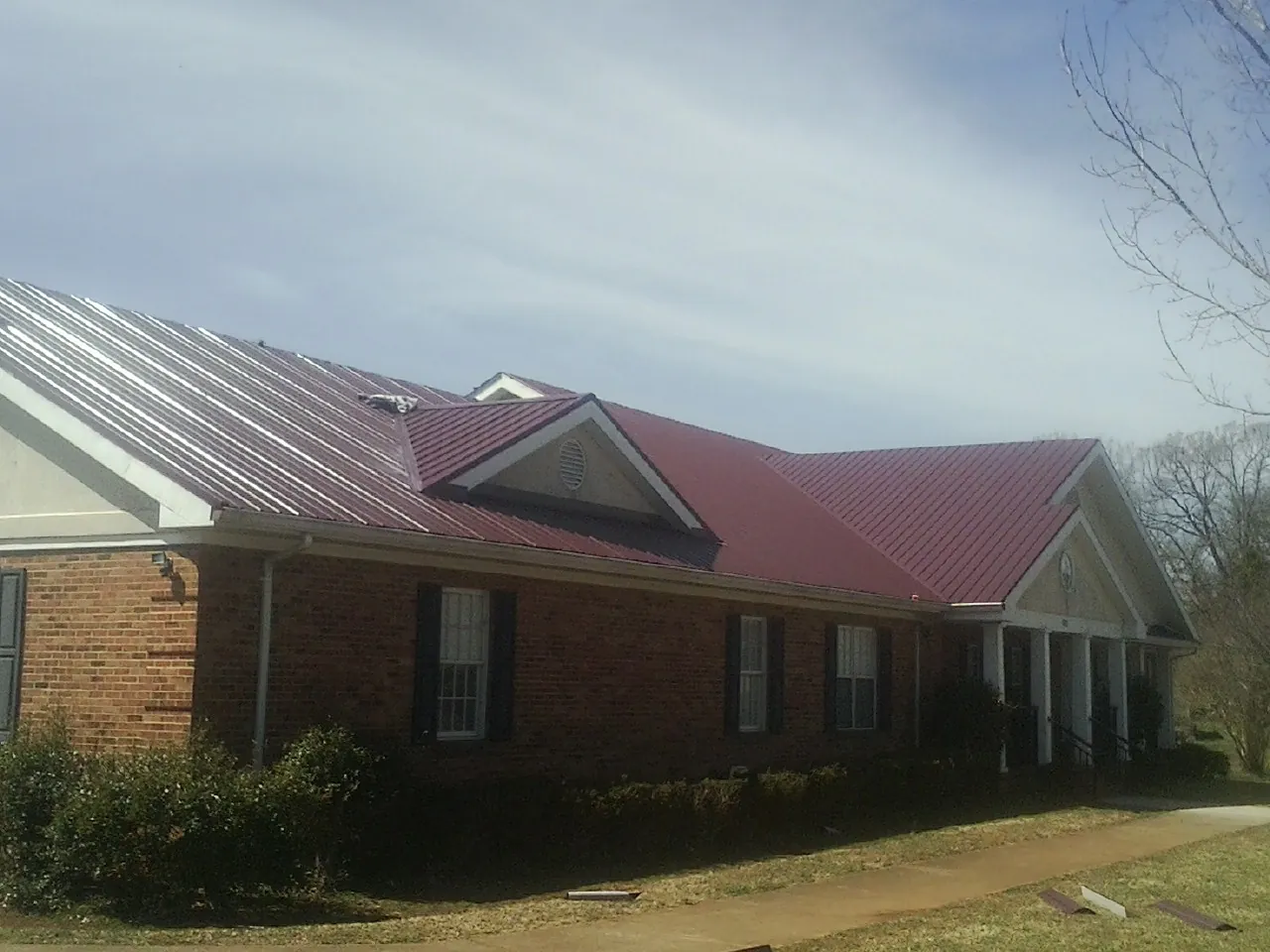 Red metal roof with gabled entries on a long brick building, from a Hail Damage Roof Repair job in Grayland