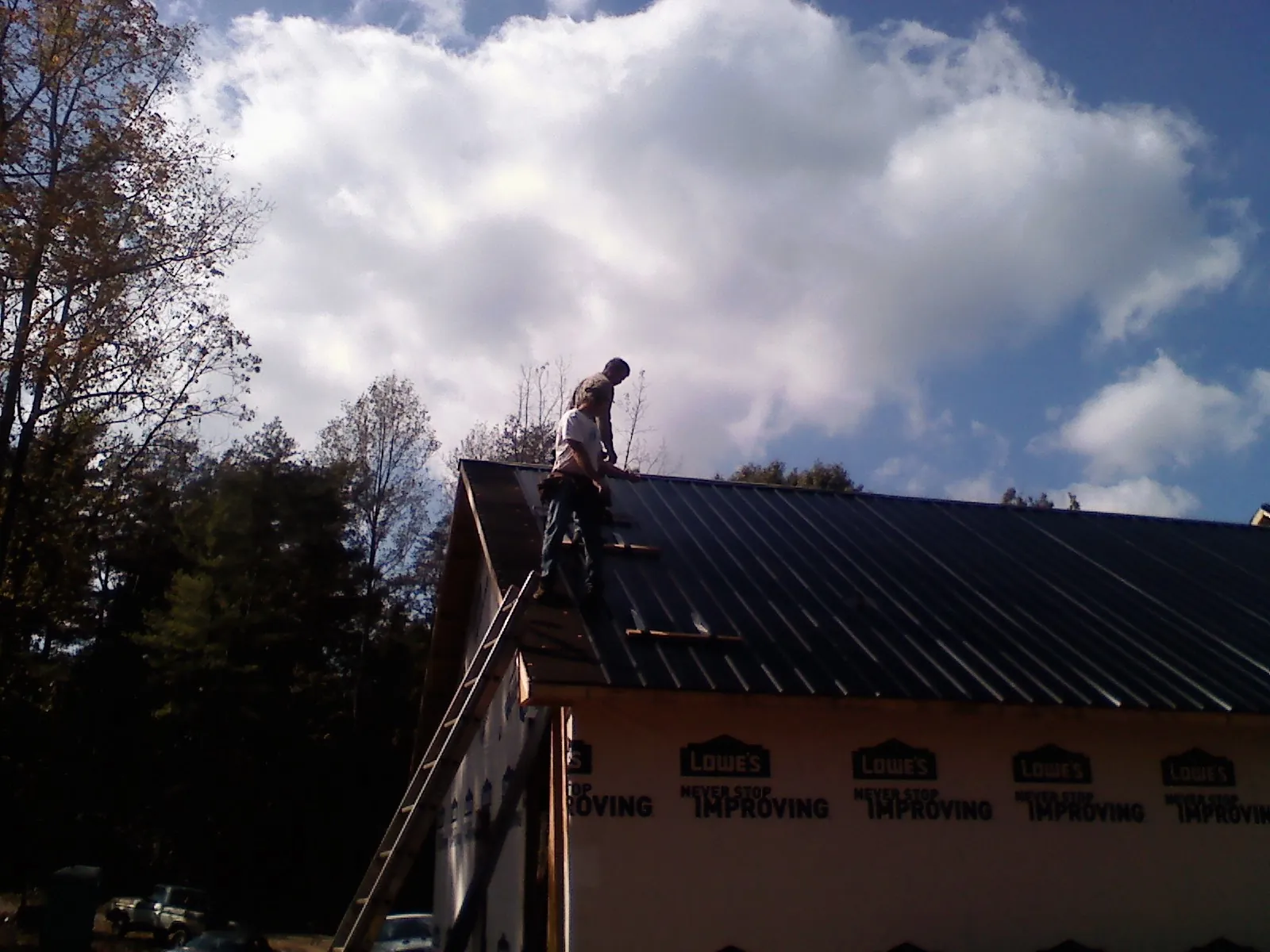 Roofer fastening dark metal panels high against a cloudy sky, from a Roof Inspection job in Grayland