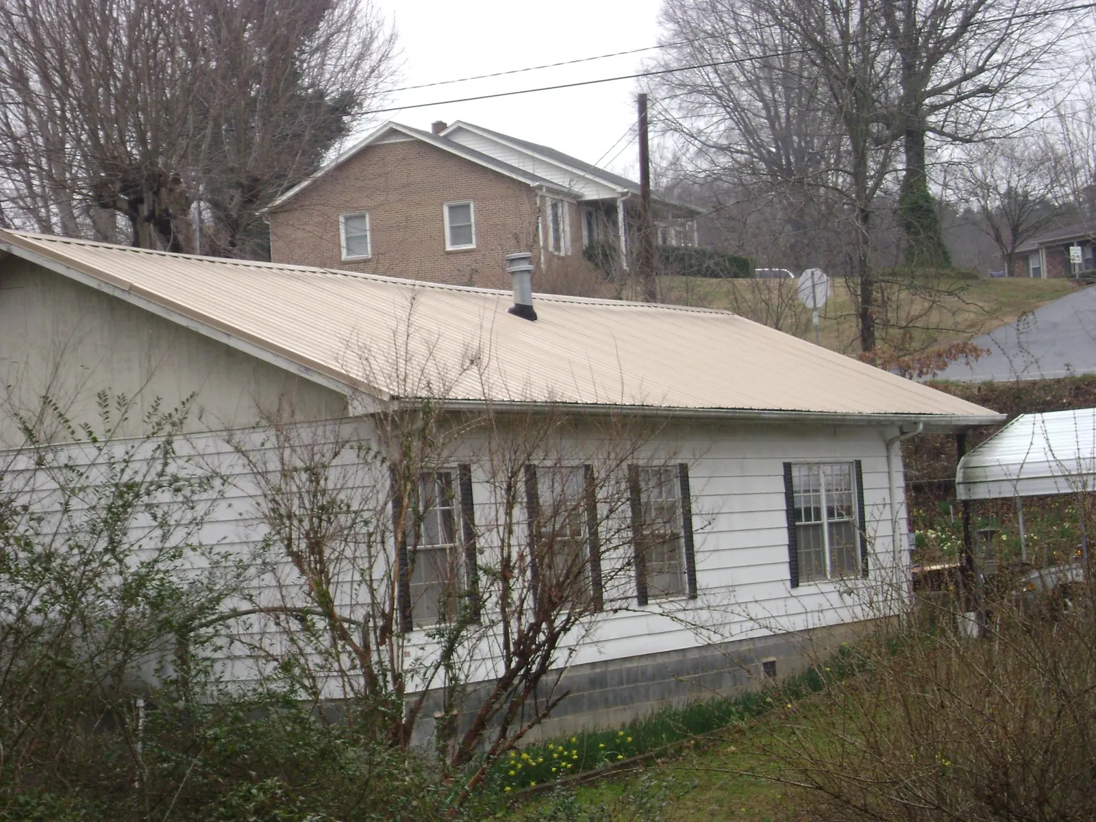Tan metal roof on a white sided house set into a hillside — Commercial Roofing by Roofing Brothers in Grayland